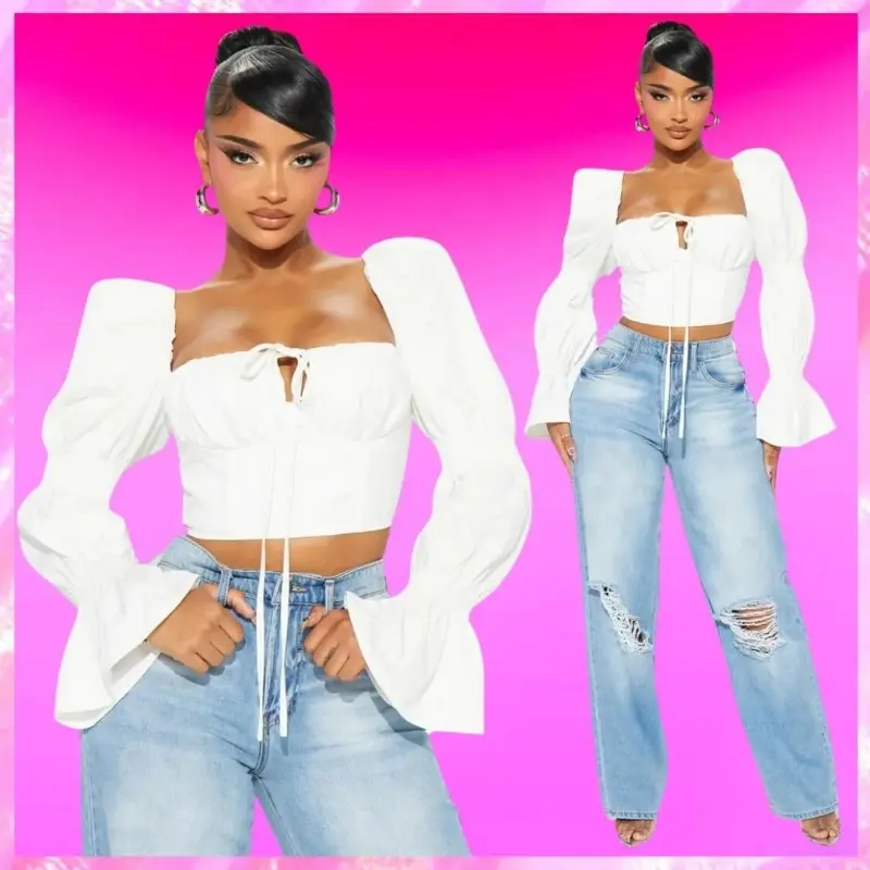 Woman wearing a white top with puffed sleeves and light blue ripped jeans, standing against a pink background.